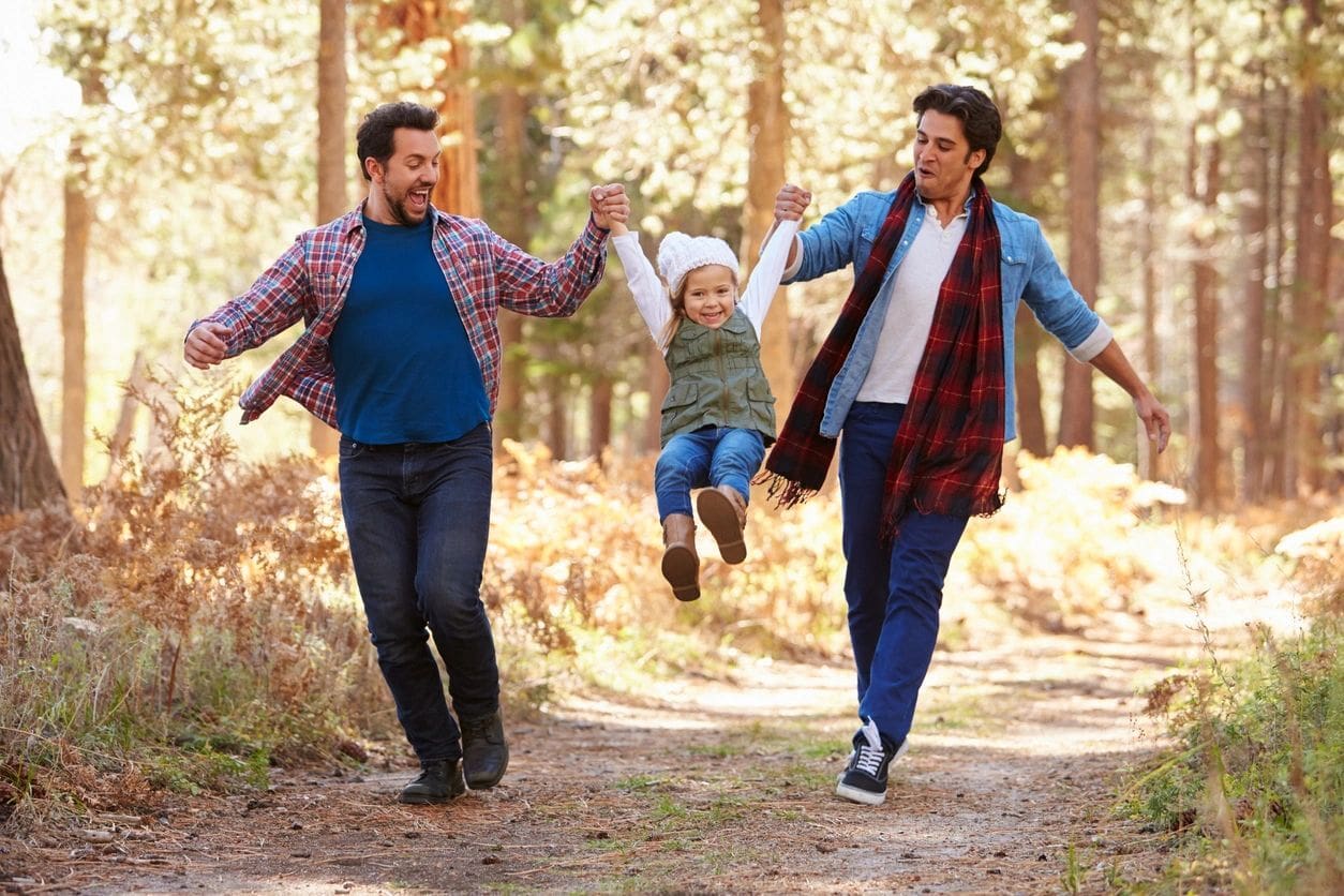 Two men holding hands while walking with a child.