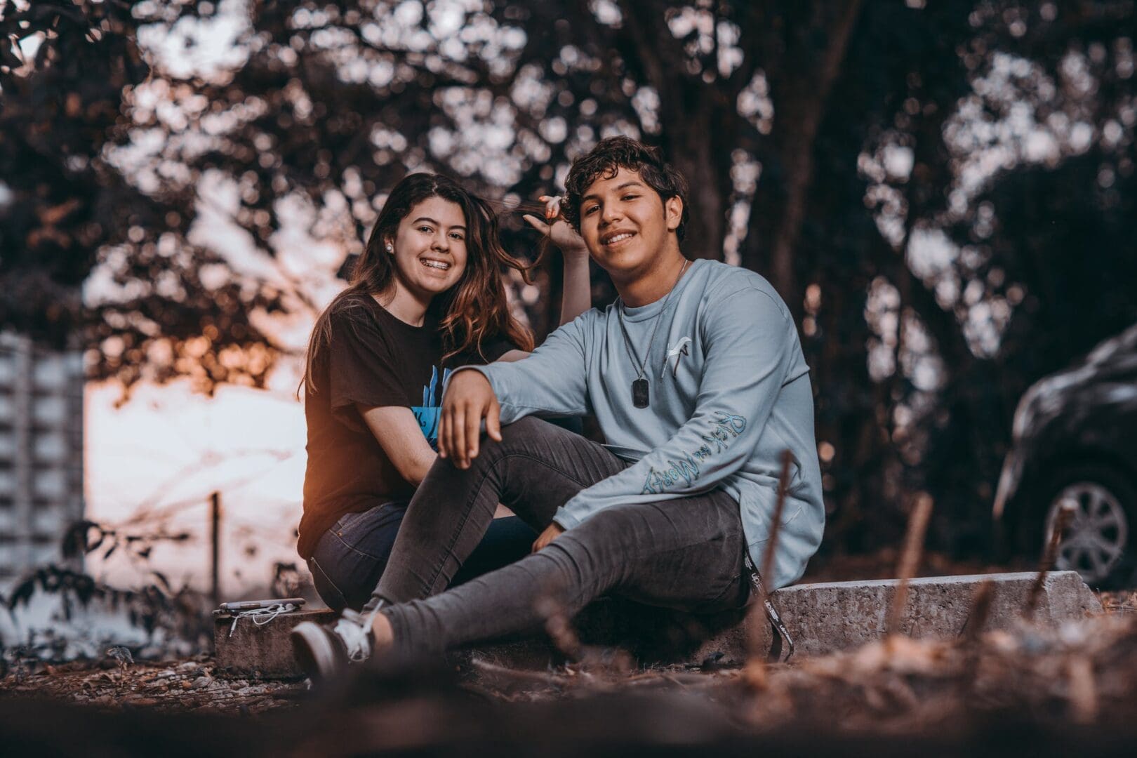 A man and woman sitting on the ground near trees.