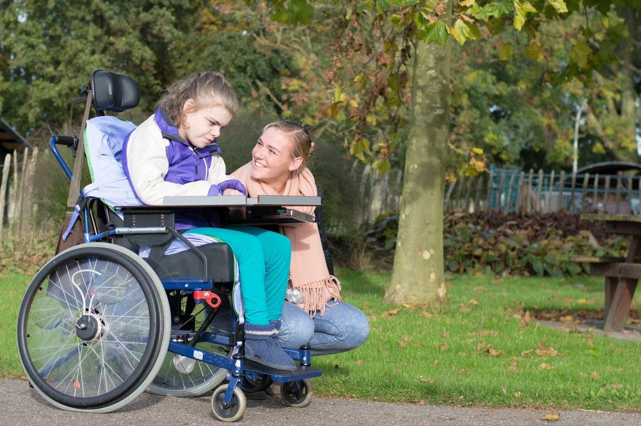 A woman and girl sitting on the ground next to a wheelchair.