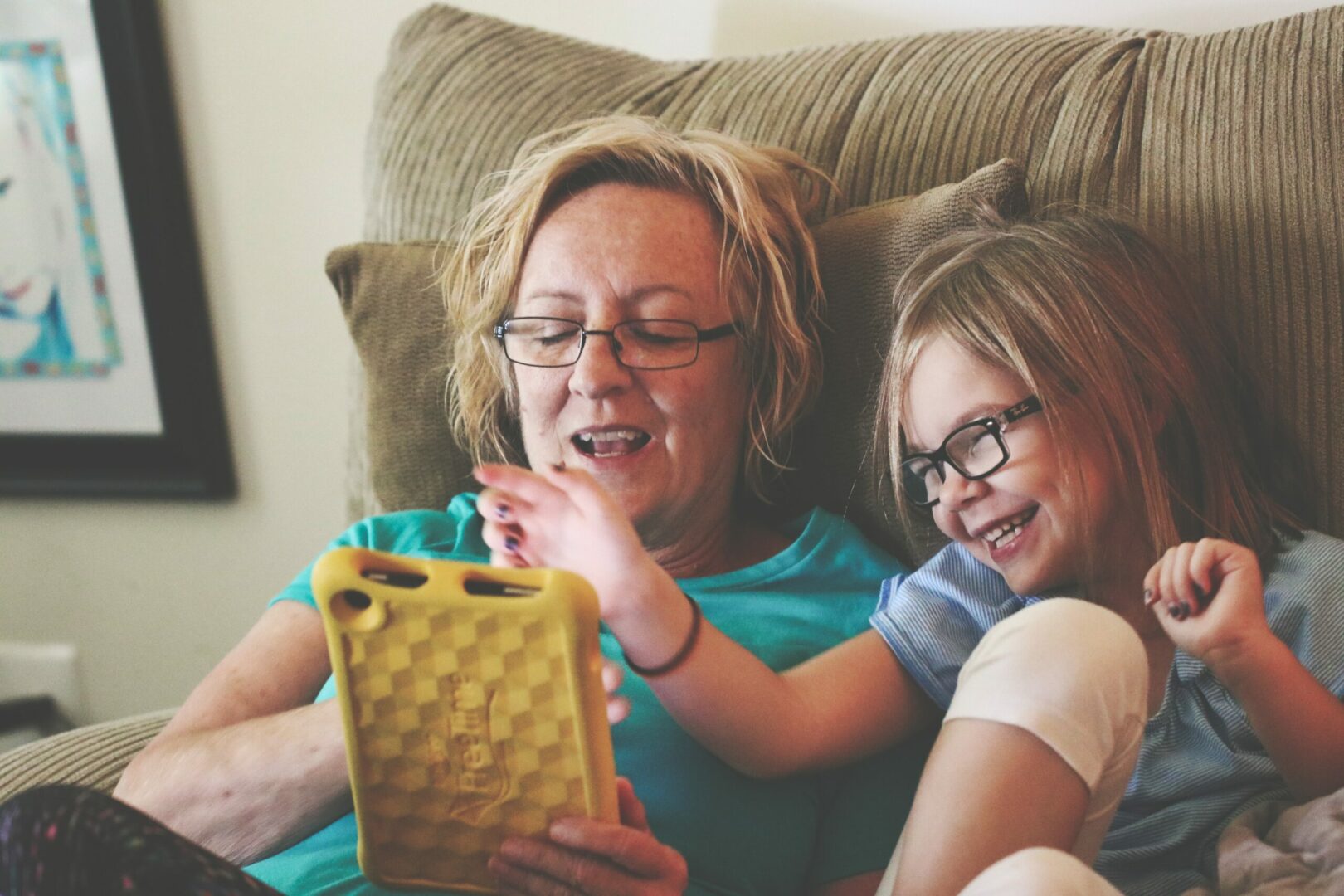 A woman and girl sitting on the couch looking at an ipad.